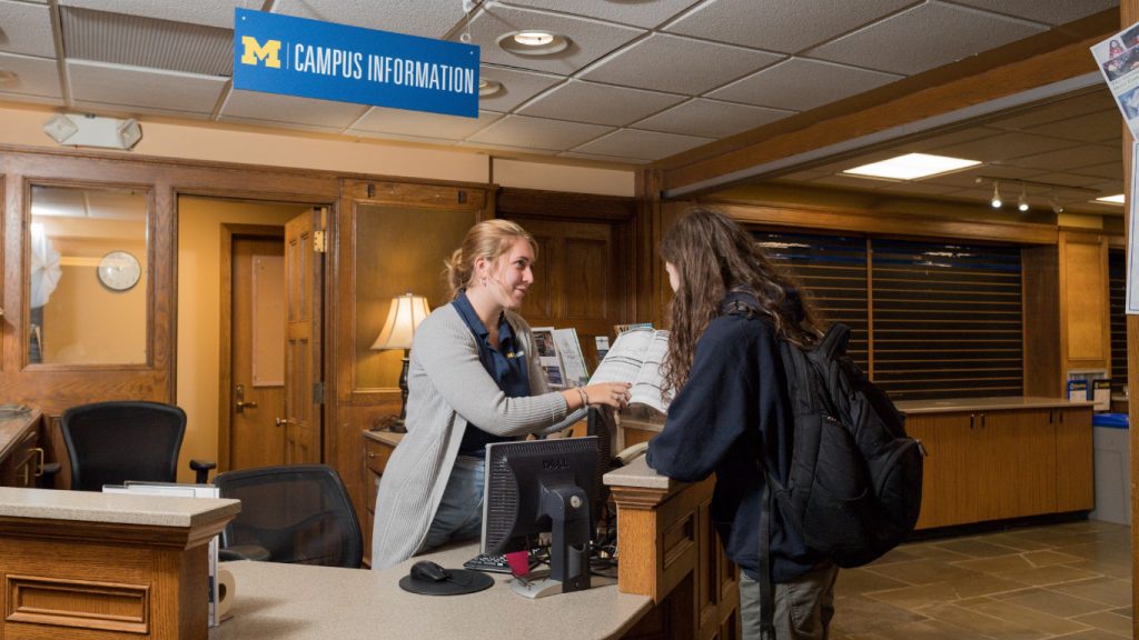Student employee helping a visitor at the Campus Information desk at the Michigan League. 